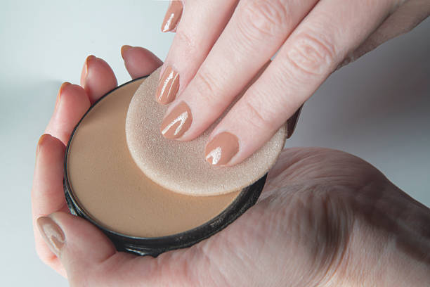 Close-up of hands applying compact powder with a sponge, illustrating makeup application technique.